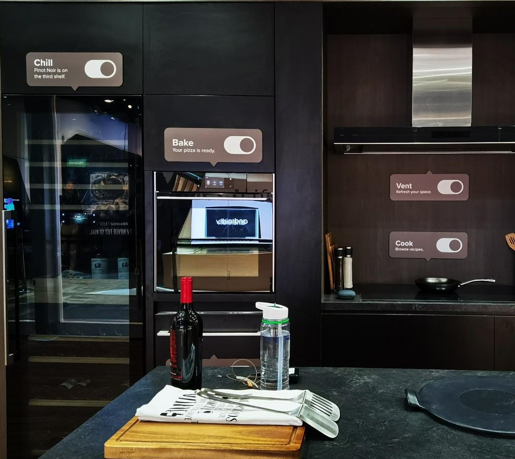 Modern dark kitchen with smart fridge, oven, vent and cook controls displayed digitally on cabinets.
