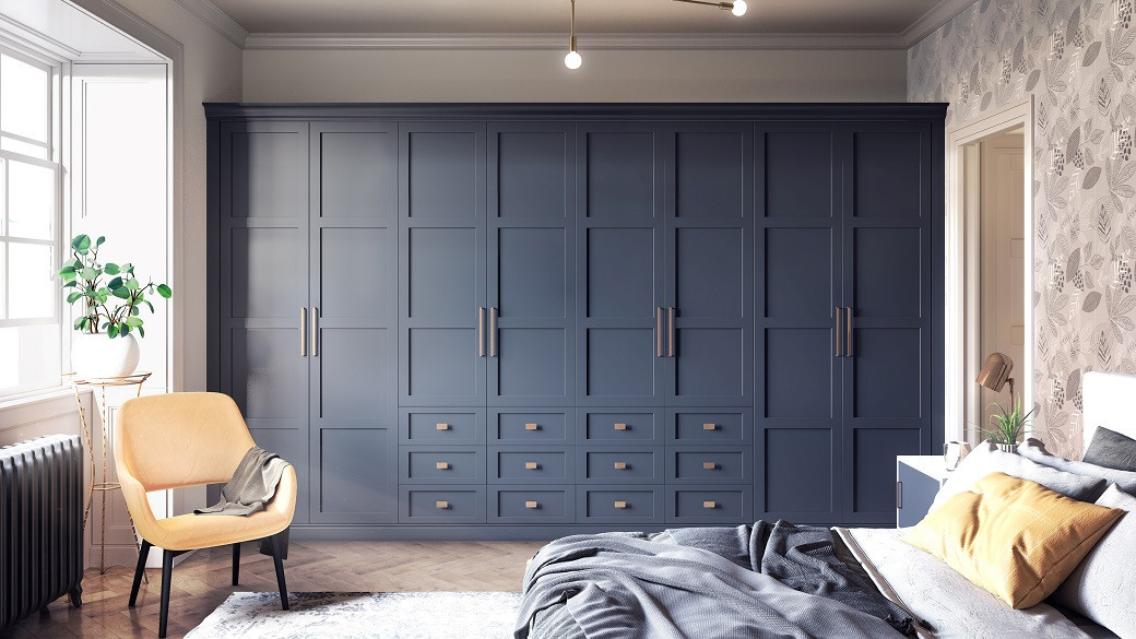 Bedroom with large matte navy blue cupboards, mustard armchair, grey bedspread, and floral wallpaper.