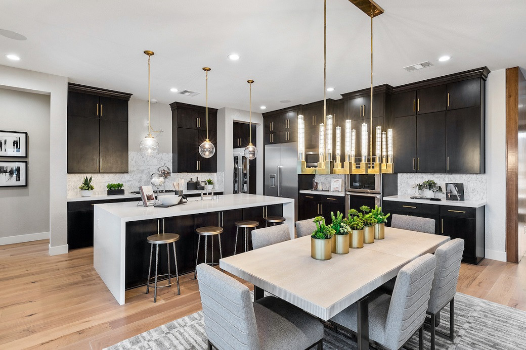 Modern kitchen with dark cabinetry, white island, four backless stools, light wood dining table, six upholstered chairs, and