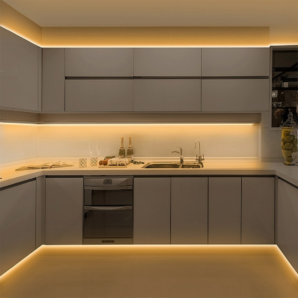 Modern kitchen with grey cabinets and warm LED strip lighting under cabinets, along ceiling edges and floor edges.