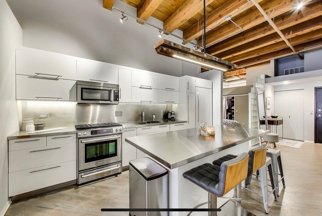 Modern kitchen with white cabinetry, stainless steel appliances and backsplash, wooden ceiling beams, and a metal island coun