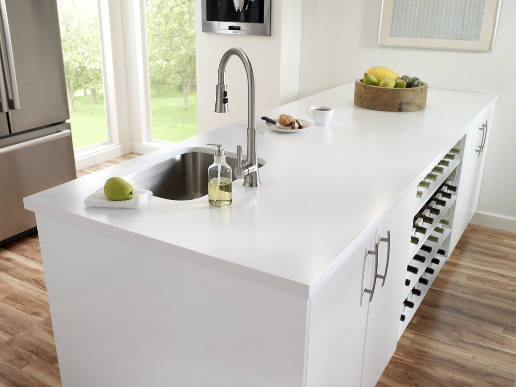 White kitchen island with a stainless steel sink, chrome faucet, soap dispenser, fruit bowl, and wine racks underneath.