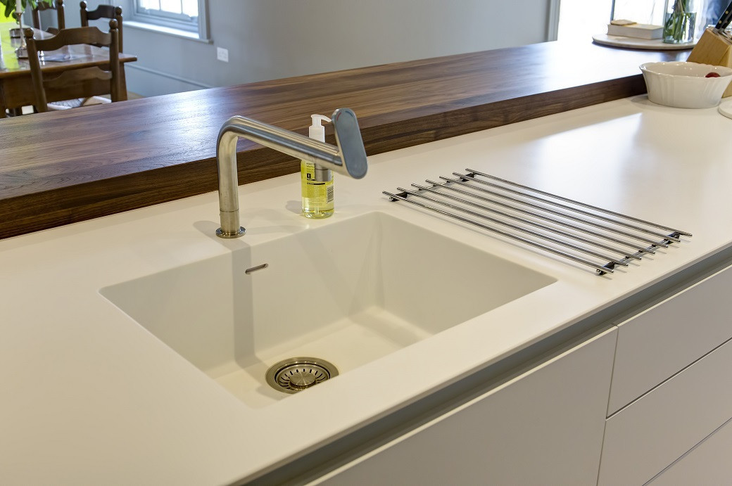 White Corian kitchen countertop with an integrated sink, a stainless steel faucet, and a wooden bar countertop in the backgro