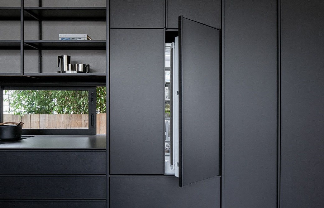 Sleek modern kitchen with matte black cabinets, an open fridge door, stainless steel kettle, pot, and a window showing greene