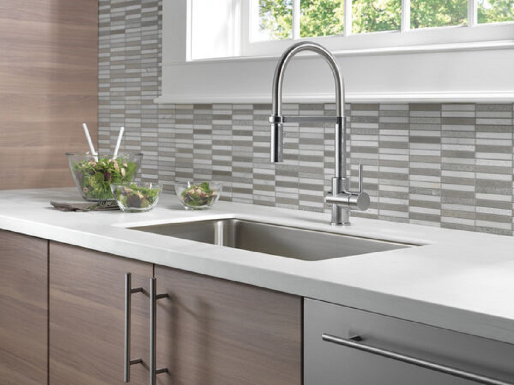 Modern kitchen sink with chrome high-arc faucet, white countertop, wooden cabinets, and salad bowls on the counter.
