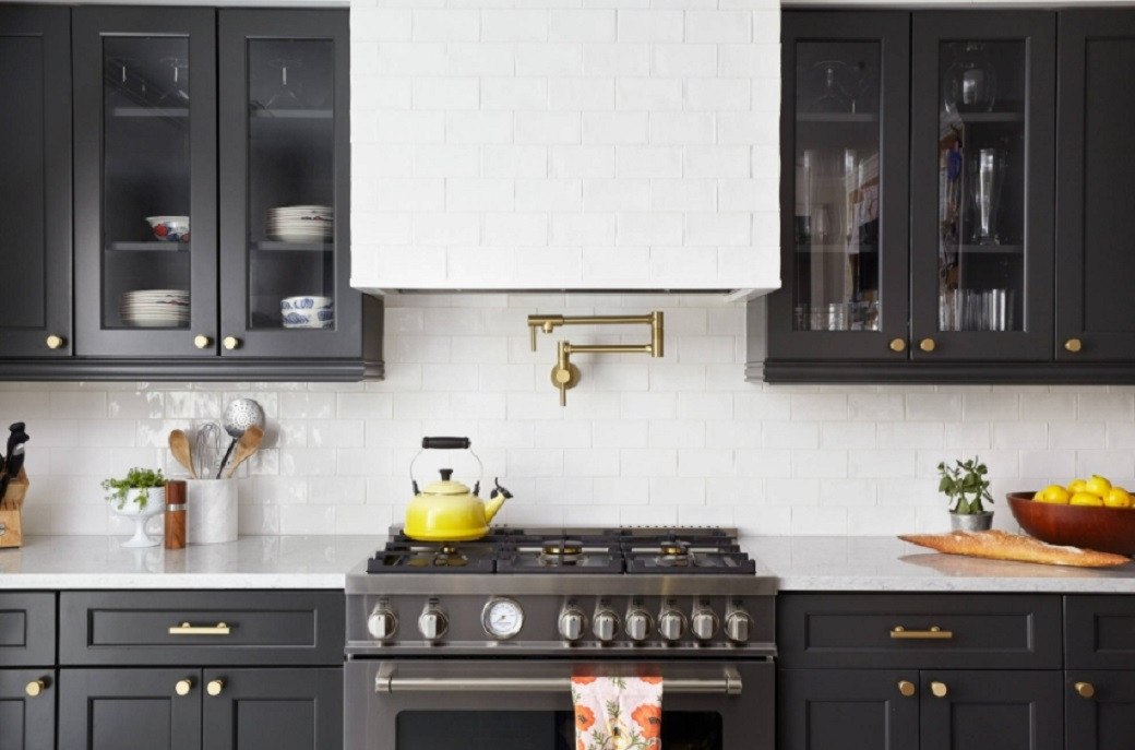 Modern kitchen with black cabinets, white subway tile backsplash, a yellow kettle on stove, and a brass pot filler above the