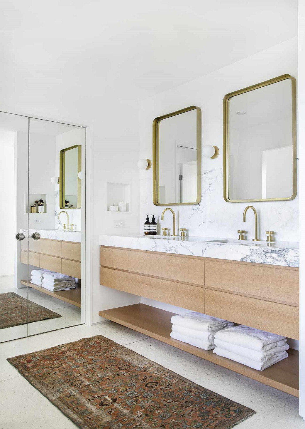 Modern bathroom with a wood floating vanity, marble countertop, two gold-framed mirrors, and a patterned rug.