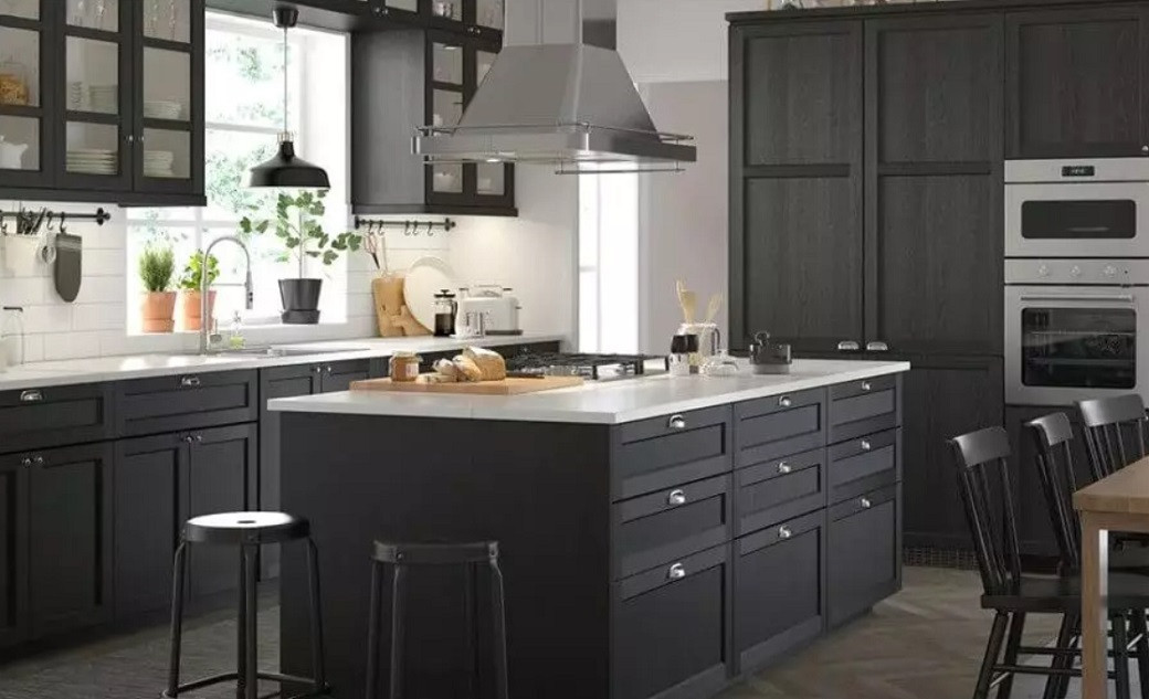 Modern kitchen with dark cabinetry, a large island with white countertop, stainless steel appliances, and two black stools.